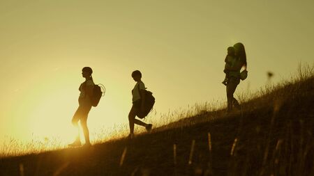 Family of tourists with children traveling at sunset. children and mom with backpacks travel down...
