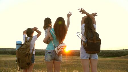 Mom travels with her daughters, admire the sunset and wave their hands. Mom and children are tourists. girls travel in the sunset light. Hiker Girl. girls travel with backpacks on a country road.の写真素材