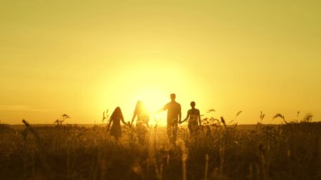 happy family walks in field in sunset light. dad mom and daughters are walking in park in the light...