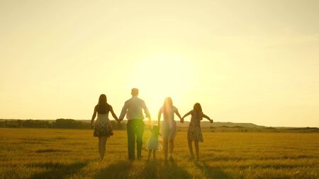 mother, father and little daughter with sisters walking in the field in the sun. Happy young family. Children, dad and mom play in the meadow in the sunshine. The concept of a happy family.の写真素材