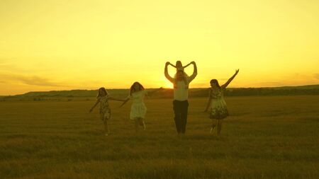 Happy young family with a child run across field in sunset light. mother, father and little daughter...