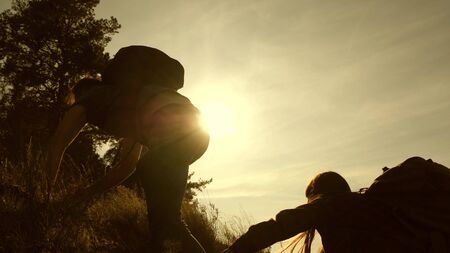 father holds out his hand helping children climb mountain. Family of tourists with kids traveling at sunset. dad, children and mom with backpacks travel climb mountain in the sun. tourist teamworkの写真素材