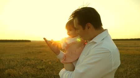 concept of happy family and childhood. father playing with his daughters resting in the park. Dad and mom playing with a little daughter in her arms at sunset. family walks with a child at sunset.の写真素材