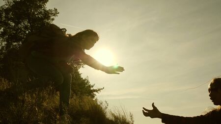women travelers climb mountain, offer each other a helping hand, helping to climb hill. tourist teamwork. Family of tourists traveling at sunset. sisters with backpacks travel climbing mountain in sunの写真素材