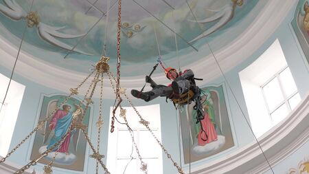 An industrial climber on a ladder is preparing a rope for lifting equipment. a worker in a protective helmet knits a knot on a rope.の写真素材