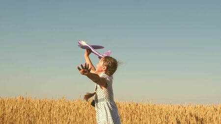 Happy girl runs with a toy airplane on a field in the sunset light. children play toy airplane. teenager dreams of flying and becoming pilot. the girl wants to become pilot and astronaut. Slow motionの写真素材