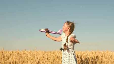 Happy girl runs with a toy airplane on a field in the sunset light. children play toy airplane. teenager dreams of flying and becoming pilot. the girl wants to become pilot and astronaut. Slow motionの写真素材
