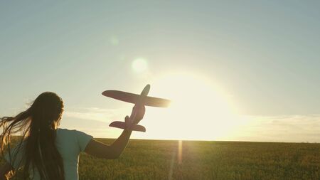 Happy girl runs with a toy airplane on a field in the sunset light. children play toy airplane. teenager dreams of flying and becoming pilot. the girl wants to become pilot and astronaut. Slow motionの写真素材