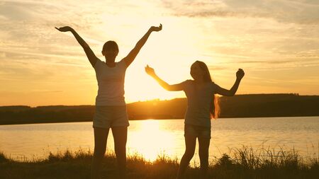 happy girls dancing on the beach. party by the lake, children dancing. beautiful girls having fun listening to music. sisters are dancing. teens girlfriends holiday disco.の写真素材