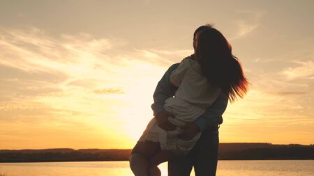 Happy guy and girl waltz in the evening in the summer park. Loving man and woman dance in bright rays of sun on the background of the lake. Young couple dancing at sunset on beach.の写真素材