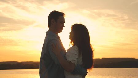 Young couple dancing at sunset on beach. Loving man and woman dance in bright rays of sun on the background of the lake. Happy guy and girl waltz in the evening in the summer park.の写真素材