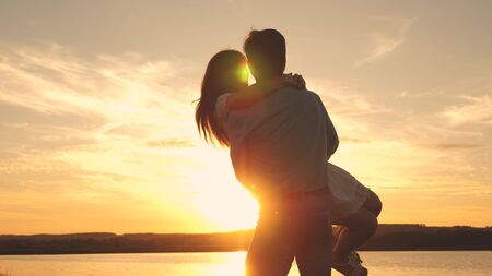 Happy guy and girl waltz in the evening in the summer park. Loving man and woman dance in bright rays of sun on the background of the lake. Young couple dancing at sunset on beach.の写真素材