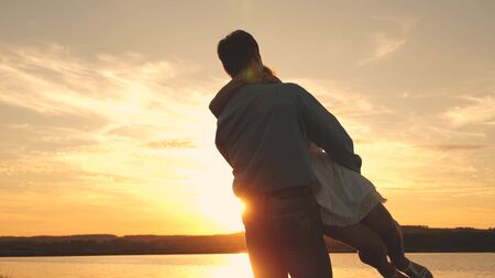 Happy guy and girl waltz in the evening in the summer park. Loving man and woman dance in bright rays of sun on the background of the lake. Young couple dancing at sunset on beach.の写真素材