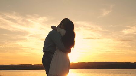 Happy guy and girl waltz in the evening in the summer park. Loving man and woman dance in bright rays of sun on the background of the lake. Young couple dancing at sunset on beach.の写真素材