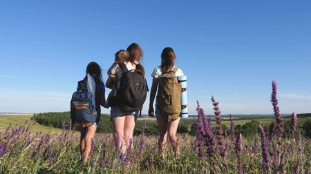 Mom and daughters, children travel across the field with backpacks in summer colors. Family on vacation. Tourist girls and a little baby go camping in the forest. Teamwork travelersの写真素材