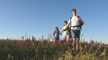 teamwork of tourists. travelers go with backpacks through the meadow. Family of tourists with children in the countryside. travelers admire the beautiful scenery and nature. movement to victory.の写真素材