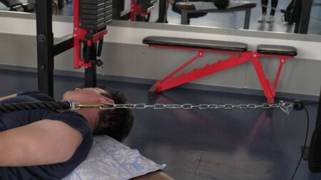 Strong muscular athlete in a t-shirt and shorts performs exercises while Pullover on lower block lying on a horizontal bench. training in a fitness club. gym workout. Sport lifestyle concept.の写真素材