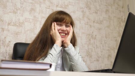 cheerful business woman sits in black leather chair talking and laughing and singing song in workplace at table. happy girl sitting in the office with laptop. woman businesswoman resting at work.の写真素材
