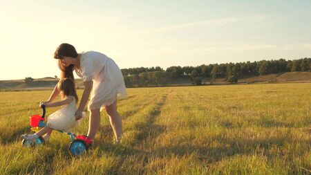 Mom teaches daughter to ride a bike. Mother plays with her little daughter. small child learns to ride a bike. concept of happy childhood.の写真素材