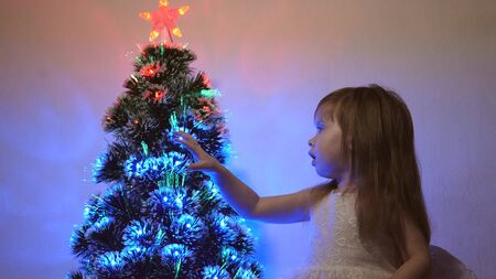 small child plays by Christmas tree in childrens room. daughter examines garland on Christmas tree. beautiful artificial christmas tree . happy childhood concept. Family plays for Christmas holidaysの写真素材