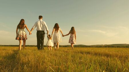 concept of a happy childhood. mother, father and little daughter with sisters walking in field in sun. Happy young family. Children, dad and mom play in meadow in sunshine. concept of happy family.の写真素材
