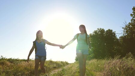 teamwork tourists teenagers. Woman travelers walk on road in the countryside. happy hiker girl in summer park. Happy girls travelers go with backpacks in field. teenager girl adventures on vacation.の写真素材