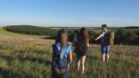 travelers admire the beautiful scenery and nature. teamwork of tourists. travelers go with backpacks through the meadow. Family of tourists with children in the countryside. movement to victory.の写真素材