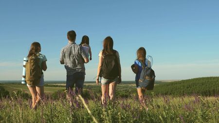 travelers admire the beautiful scenery and nature. teamwork of tourists. travelers go with backpacks through meadow. Family of tourists with children in the countryside. movement to victory.の写真素材