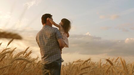 little daughter on fathers shoulders. happy child and father are playing in field of ripening wheat. baby boy and dad travel on field. kid and parent play in nature. happy family and childhood conceptの写真素材