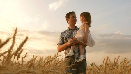 child in the arms of the father. little daughter and father are playing in a field of ripening wheat. baby boy and dad travel on field. kid and parent play in nature. happy family and childhood conceptの写真素材