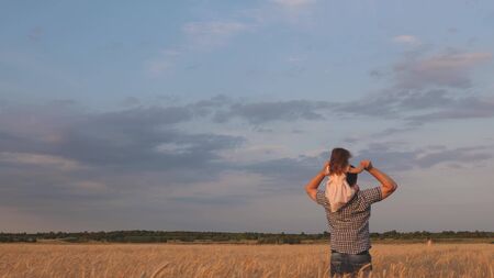 little happy daughter on fathers shoulders in field against the blue sky. baby boy and dad travel on a wheat field. child and parent play in nature. happy family and childhood concept. Slow motionの写真素材