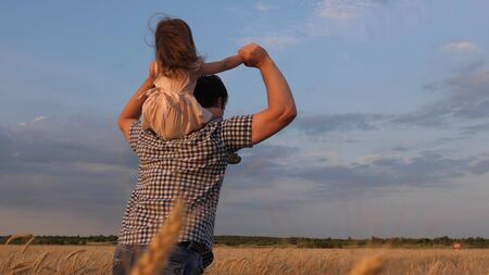 child and parent play in nature. little happy daughter on father's shoulders in field against the blue sky. baby boy and dad travel on a wheat field. happy family and childhood concept. Slow motionの写真素材