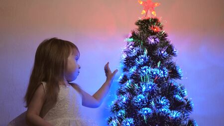 small child plays by Christmas tree in childrens room. daughter examines garland on Christmas tree. beautiful artificial christmas tree . happy childhood concept. Family plays for Christmas holidaysの写真素材