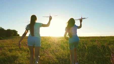 Happy childhood concept. Dreams of flying. Two girls play with toy plane at sunset. Children on background of sun with an airplane in hand. Silhouette of children playing on planeの写真素材