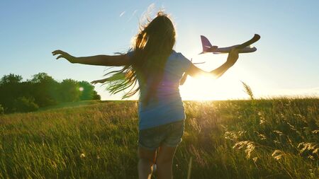 Happy childhood concept. Dreams of flying. Two girls play with toy plane at sunset. Children on background of sun with an airplane in hand. Silhouette of children playing on planeの写真素材