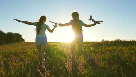 Happy childhood concept. Dreams of flying. Two girls play with toy plane at sunset. Children on background of sun with an airplane in hand. Silhouette of children playing on planeの写真素材