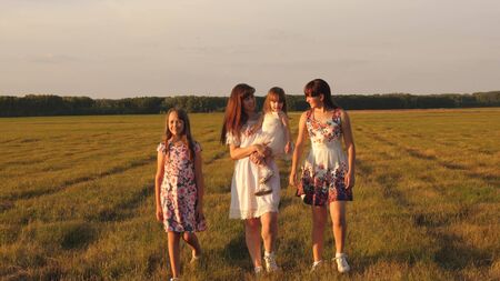 Children and mom are playing in the meadow. concept of a happy family. mother and little daughter with sisters walking in park. Happy young family with a child walking on a summer field.の写真素材