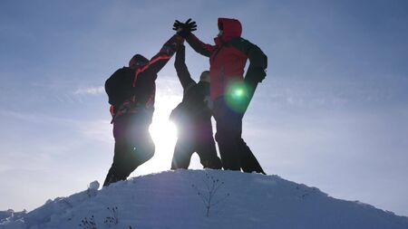 travelers met on top of success. Tourists come to top of snowy hill and rejoice at victory against backdrop of yellow sunset. teamwork and victory. team work of people in difficult conditionsの写真素材