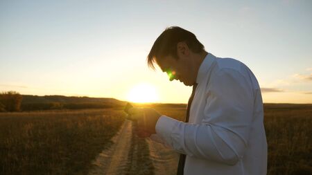 businessman playing tablet games in the park in the warm rays of the sunset. man playing games on the smartphone. happy man in white shirt and tie plays online on tablet.の写真素材