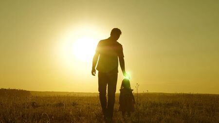 little daughter and dad walk around field holding hands. child holds father's hand. dad and baby are resting in park. child plays with his father. happy family and childhood conceptの写真素材