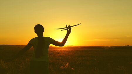 children play toy airplane. Happy girl runs with a toy airplane on a field in the sunset light. teenager dreams of flying and becoming pilot. the girl wants to become a pilot and astronaut.の写真素材
