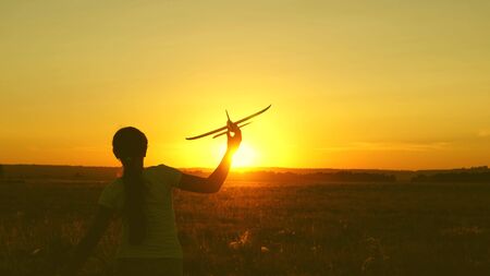 children play toy airplane. Happy girl runs with a toy airplane on a field in the sunset light. teenager dreams of flying and becoming pilot. the girl wants to become pilot and astronaut.の写真素材