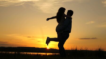Young couple dancing at sunset on beach. Happy guy and girl waltz in evening in the summer park. Loving man and woman dance in bright rays of sun on the background of the lake.の写真素材
