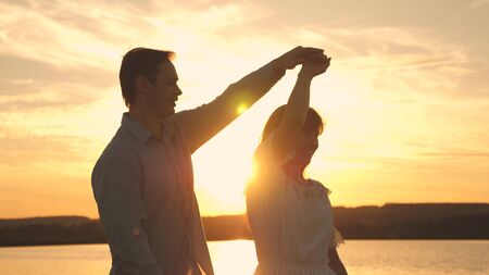 Loving man and woman dance in bright rays of sun on the background of the lake. Young couple dancing at sunset on beach. Happy guy and girl waltz in the evening in the summer park.の写真素材