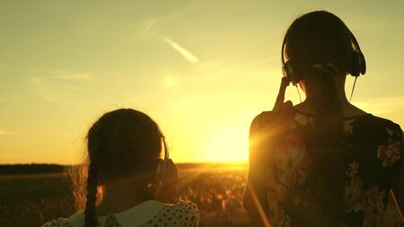 Free girls travel listen to music and dancing in rays of a beautiful sunset in the park. teenagers travelers with headphones enjoy the rays of a warm sunset. women listen to music togetherの写真素材