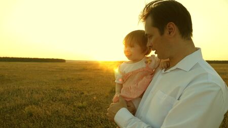 father teaches little daughter in the park. concept of happy family and childhood. Dad playing with a little daughter in her arms at sunset. family walks with the child at sunsetの写真素材