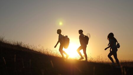 children and mom with backpacks travel climb mountain in sun. mom and daughters go camping. Family of tourists with kids traveling at sunset. joint work of tourists. movement to victory.の写真素材