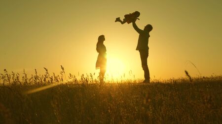 child, dad and mom play in meadow in the sun. concept of a happy childhood. mother, father and little daughter walking in a field in the sun. Happy young family. concept of a happy family.の写真素材