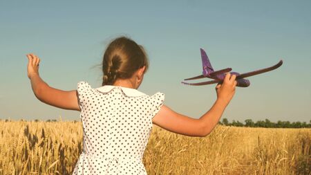 Happy girl runs with a toy airplane on a field in the sunset light. children play toy airplane. teenager dreams of flying and becoming a pilot. girl wants to become a pilot and astronaut. Slow motionの写真素材