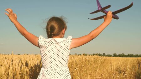 Happy girl runs with a toy airplane on a field in the sunset light. children play toy airplane. teenager dreams of flying and becoming a pilot. girl wants to become a pilot and astronaut. Slow motionの写真素材